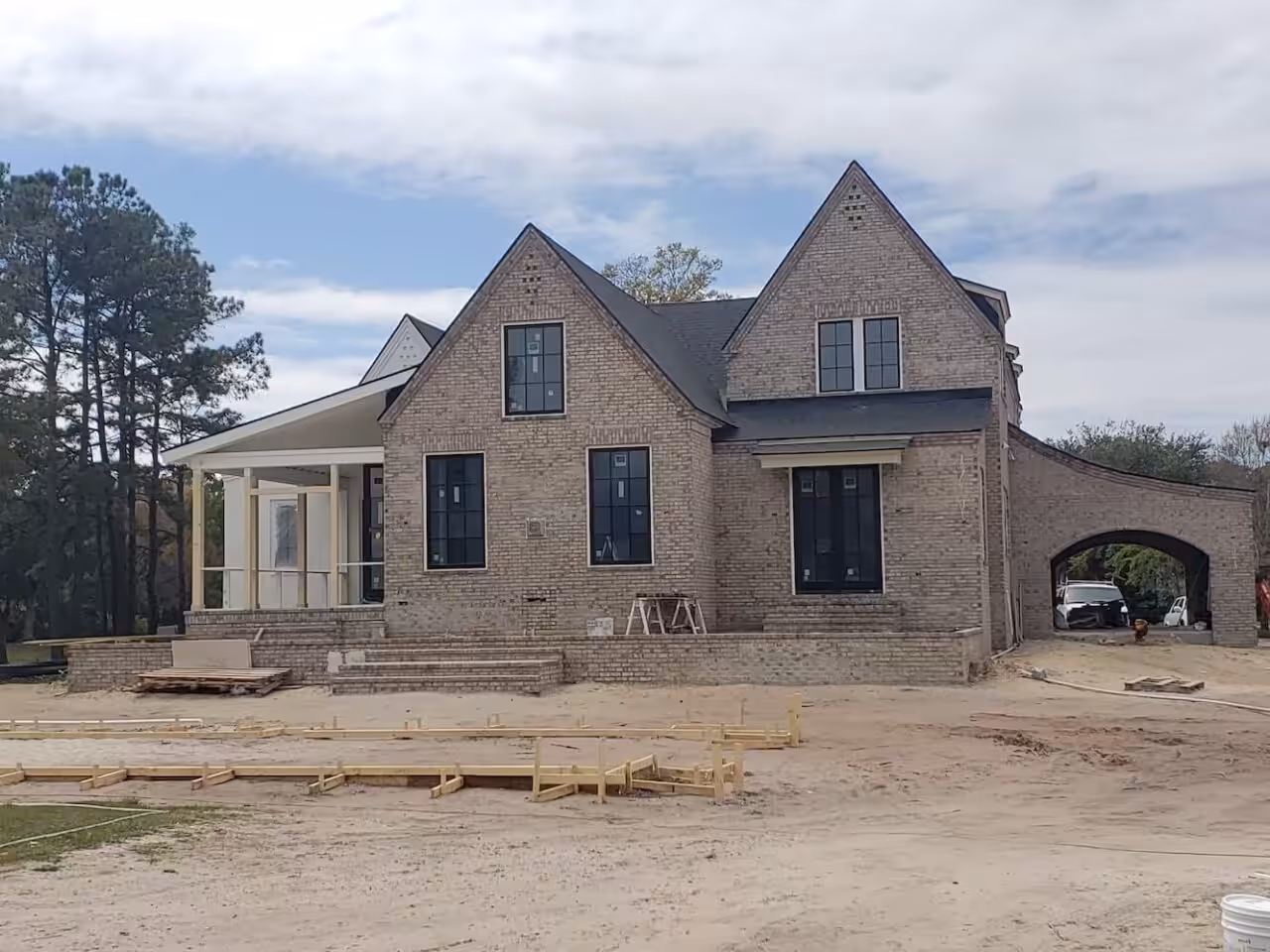 Painting a Brick Exterior: The Numbers to Check Before the First Coat New two-gable house with bare tan brick walls, an arched carport and a sandy unfinished yard in March 2019