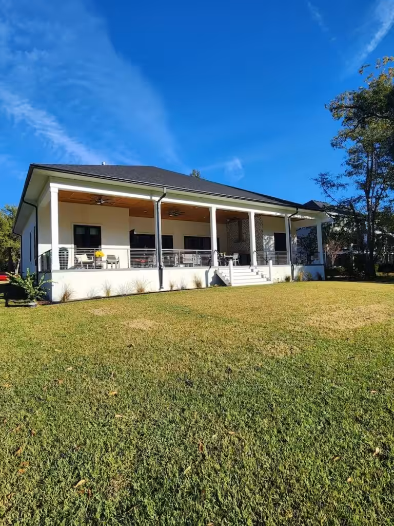 Painting a House Before Selling: A Decision Guide for Charleston Sellers White one-story house with a long front porch, square columns and a dark roof, seen across a green lawn